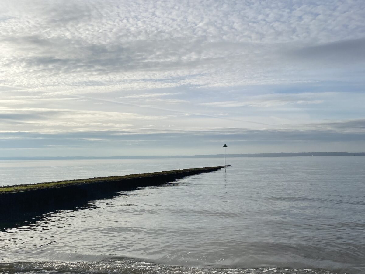 Calm waters at Hill Head beach's concrete covered waste water pipe and steel marker